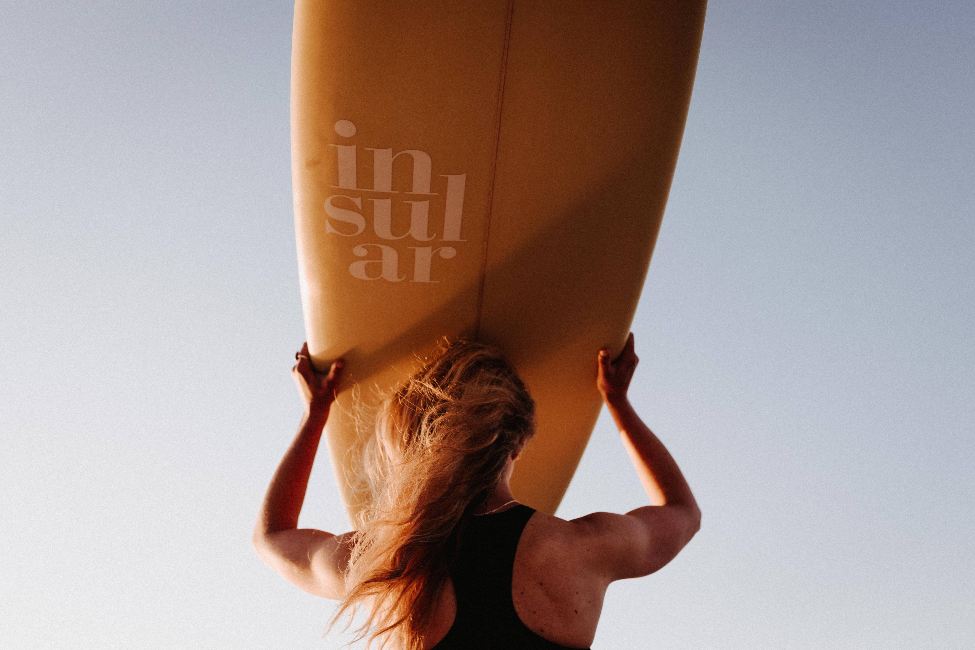 Frau trägt Surfbrett auf dem Kopf